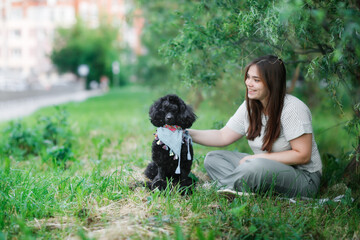 Charming plus size girl with long brown hair with a dog in a park in nature, a young woman and a pet black poodle