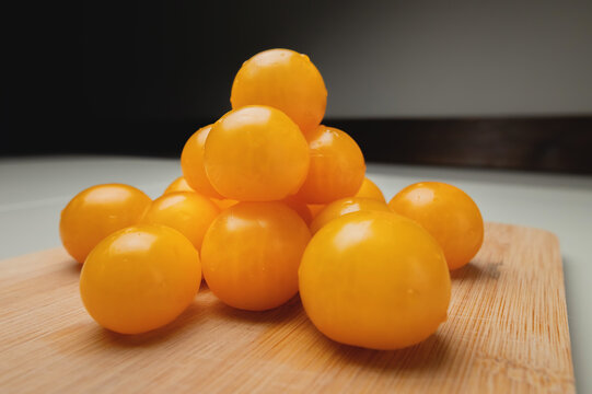 Close-up shot of yellow cherry tomatoes on a wooden cutting board in the kitchen on a white table