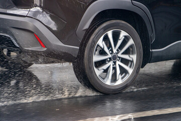 Fototapeta na wymiar Detail of the rear wheel of a car driving in the rain on a wet road.