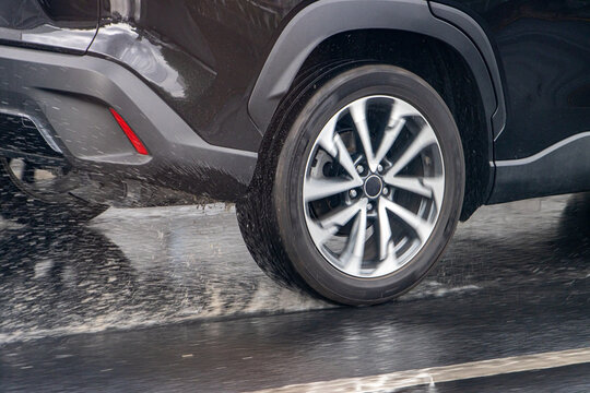 Detail of the rear wheel of a car driving in the rain on a wet road.