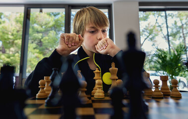 Concentrated boy developing chess strategy, playing board game with teacher at chess class