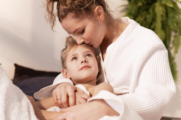 Young mom cuddling hugging cute little girl after bath, showing love and affection. Happy mother...