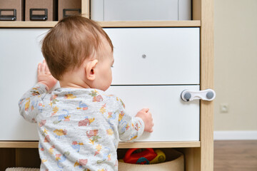 Toddler baby boy rips off a cabinet drawer with his hand. The child holds the cabinet door handle,...