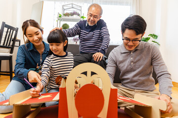 Asian little child girl playing with cardboard toy airplane handicraft  at home in living room .Happy little girl sit on floor in new home drawing painting together.