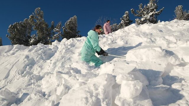 Snowboarder digging snow with shovel on the slope of  ski resort