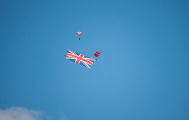 parachute display team member towing a large union flag in descent, blue sky