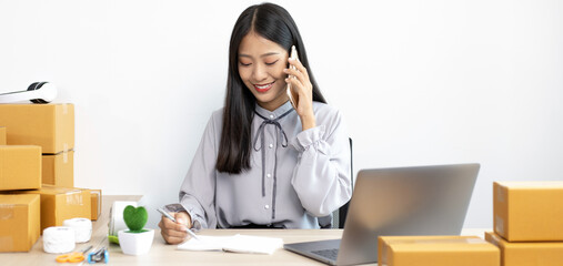 Asian businesswoman is taking online orders from a phone and chatting with customers to confirm...