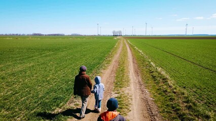 Sad family of ukrainian refugees with children and suitcase walking away from russian invasion by road between fields. Concept of peaceful and carefree life without armed conflicts
