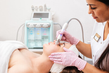 Beauty salon. The cosmetologist in medical gloves doing a hydra peeling procedure on the client's...