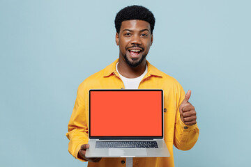 Young happy man of African American ethnicity 20s wear yellow shirt hold use work on laptop pc computer with blank screen workspace area show thumb up isolated on plain pastel light blue background.
