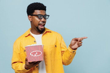 Young man of African American ethnicity in 3d glasses watch movie film hold bucket of popcorn point...