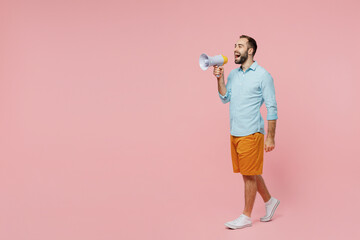Full body side view young smiling man 20s wearing classic blue shirt hold scream in megaphone announces discounts sale Hurry up go walk isolated on plain pastel light pink background studio portrait