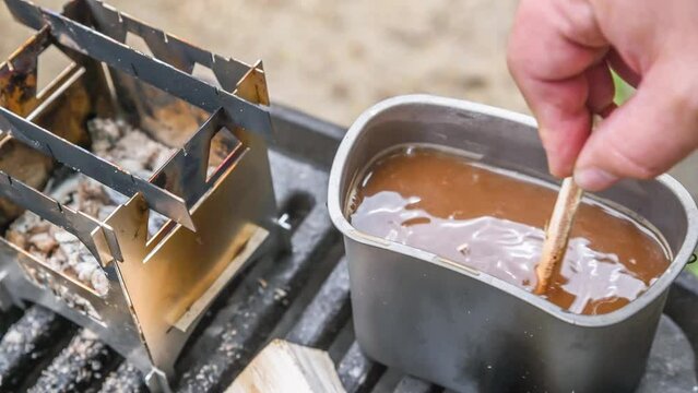 Filmmaterial von brennendem Edelstahl Hobo Kocher mit Titan Becher wird Kaffee mit einem Holzst&uuml;ck umger&uuml;hrt auf einem Grill im Freien, Deutschland