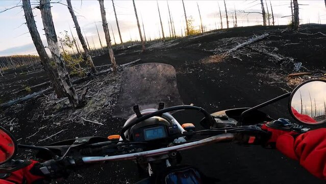 motorcyclist riding offroad through the dead forest volcano territory. Driver's view from behind the wheel