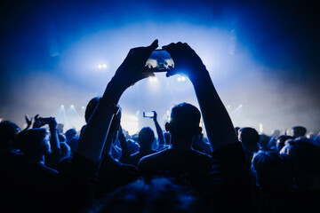 silhouettes of concert crowd in front of bright stage lights. Dark background, smoke, concert  spotlights. Group of people holding hands with mobile phones at a concert  - Powered by Adobe