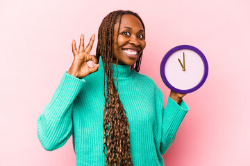 Young African American woman holding a clock isolated on pink background cheerful and confident...