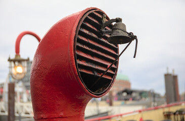 Red vintage boat vent with a small bell and some lights and a port and a city in the backround.