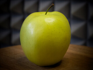 Golden Delicious is a yellow apple, one of the 15 most popular cultivars in the United States. A single apple on a wooden surface, close-up.