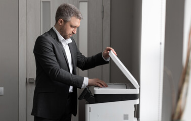 An adult successful man in a gray business suit stands near a copier