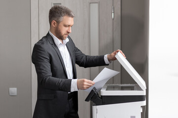An adult successful man in a gray business suit stands near a copier