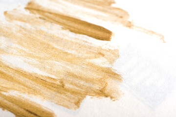 Gold metallic streaking of makeup on white background.