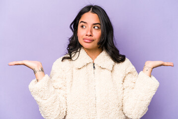 Young hispanic woman isolated on purple background confused and doubtful shrugging shoulders to...