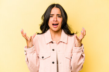 Young hispanic woman isolated on yellow background screaming to the sky, looking up, frustrated.