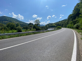 Empty country road and green mountains in summer. Cloudy blue sky
