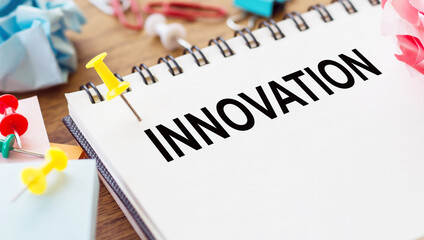 INNOVATION text on a notebook on an office desk, next to it paper needles and crumpled sheets.