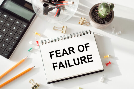 FEAR OF FAILURE text on notepad lying on office table together with calculator, cactus, pencils and paper clips and needles.