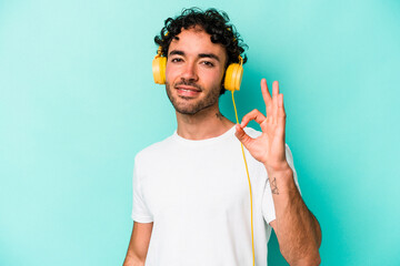 Young caucasian man listening to music isolated on blue background cheerful and confident showing...