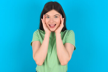 young beautiful Caucasian woman wearing green T-shirt over blue wall Pleasant looking cheerful, Happy reaction