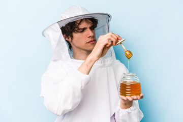 Young caucasian beekeeper man holding honey isolated on blue background