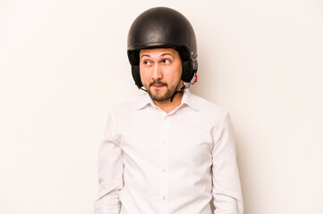 Hispanic business man going to work with motorcycle isolated on white background confused, feels doubtful and unsure.