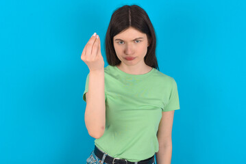 Fototapeta premium young beautiful Caucasian woman wearing green T-shirt over blue wall Doing Italian gesture with hand and fingers confident expression