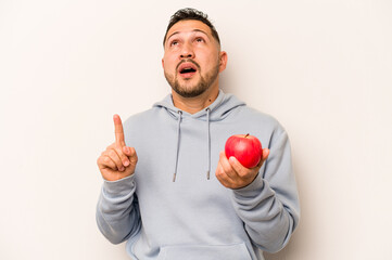 Hispanic man holding an apple isolated on white background pointing upside with opened mouth.