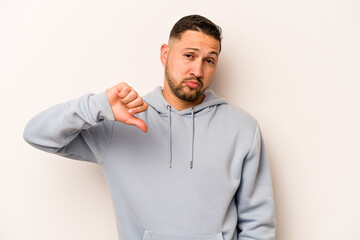 Young hispanic man isolated on white background showing a dislike gesture, thumbs down....