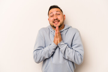 Young hispanic man isolated on white background holding hands in pray near mouth, feels confident.