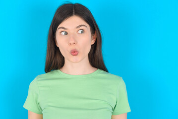Fototapeta premium Shocked young beautiful Caucasian woman wearing green T-shirt over blue wall look empty space with open mouth screaming: Oh My God! I can't believe this.