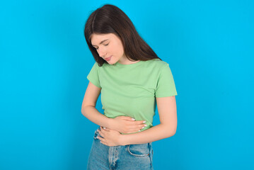 young beautiful Caucasian woman wearing green T-shirt over blue wall got stomachache