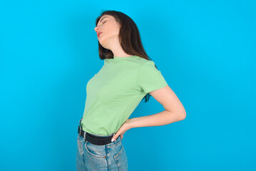 young beautiful Caucasian woman wearing green T-shirt over blue wall got back pain