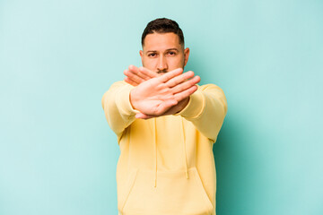 Young hispanic man isolated on blue background doing a denial gesture