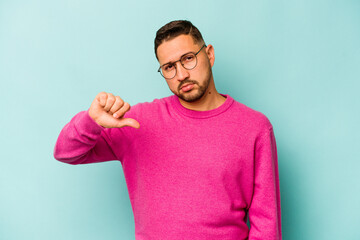 Young hispanic man isolated on blue background showing a dislike gesture, thumbs down. Disagreement...