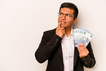 Young hispanic business man holding banknotes isolated on white background relaxed thinking about something looking at a copy space.