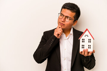 Young business hispanic man holding a little house isolated on white background looking sideways...