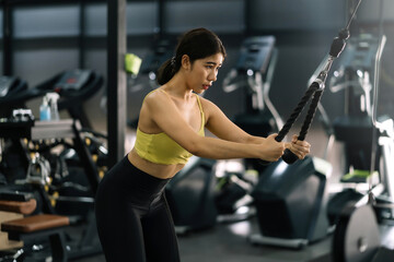 Fototapeta na wymiar Young Asian woman flexing arm muscles on cable machine at gym.
