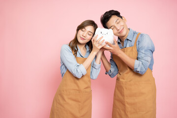 .Young Asian couple startup small business holding white piggy bank isolated on pink background