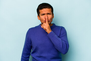 Young hispanic man isolated on blue background keeping a secret or asking for silence.