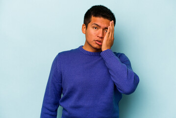 Young hispanic man isolated on blue background tired and very sleepy keeping hand on head.