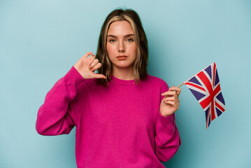 Young caucasian woman holding a English flag isolated on blue background showing a dislike gesture,...